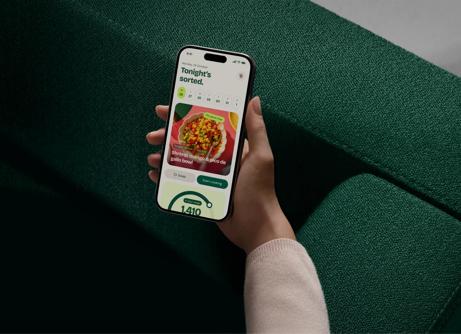 A hand holding a phone showing tonight’s dinner in Olly, over a green sofa